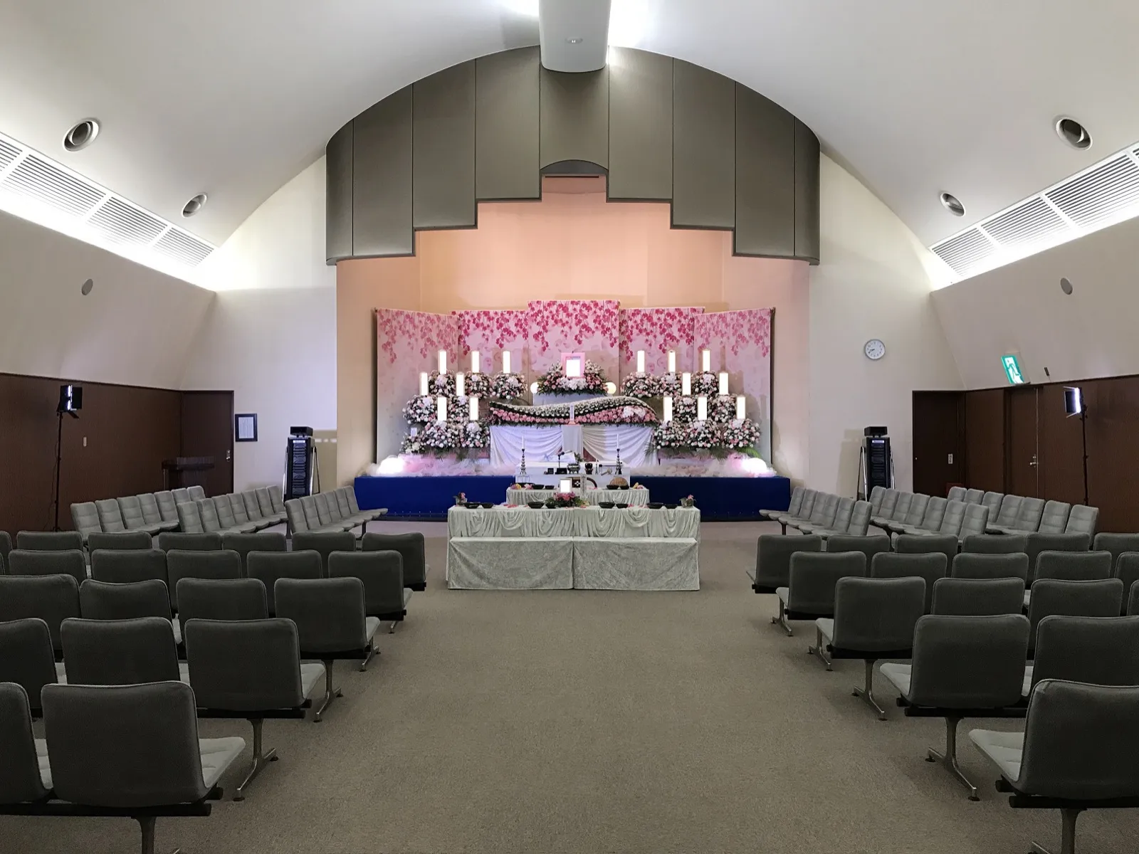 藤沢市斎場の大ホール。アーチ形の天井の下に、花の祭壇と会葬者席の椅子が並ぶ